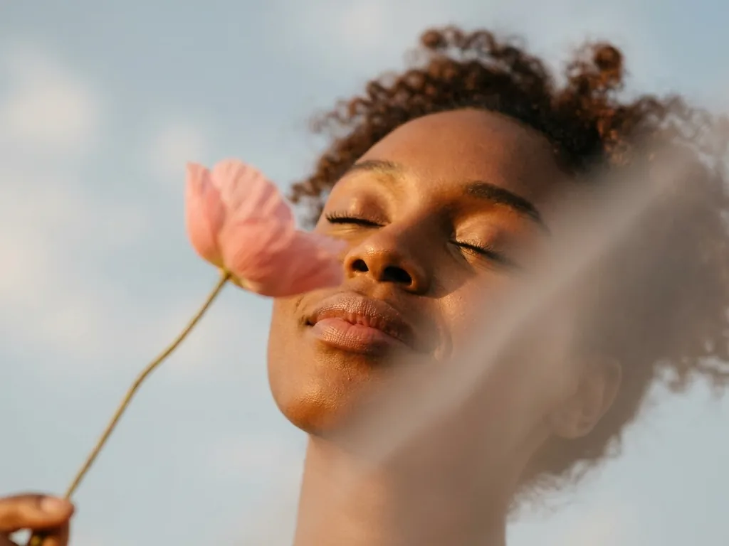 A woman with eyes closed holding a flower to her face in the sun